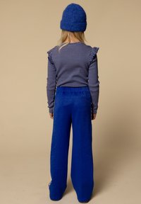 Langsleeve gestreepte top met ruches op de schouders, gecombineerd met ruime blauwe textuur broek en een bijpassende blauwe gebreide muts.