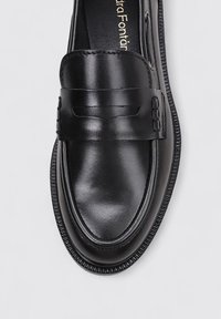 Mocasines de cuero negro con textura suave, que presentan una correa frontal y costuras detalladas a lo largo del borde para un refuerzo adicional.