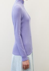 Haut violet ajusté à manches longues avec col montant et détail zippé, en tissu côtelé. Présente une texture lisse et une coupe moulante.