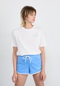 Weißes Baumwoll-T-Shirt mit einem kleinen grünen und blauen Logo, kombiniert mit hellblauen Shorts mit Kordelzug, die einen weißen Saum und passende Logodetails aufweisen.