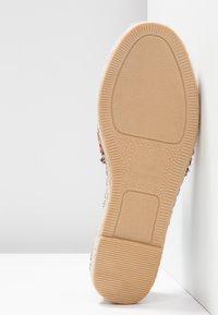 Semelle en caoutchouc beige clair avec un motif texturé. La tige présente un tissu tissé multicolore mélangé avec des tons de rouge, de noir et de crème.