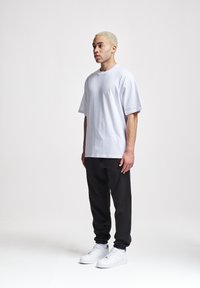 Weißes, oversized T-Shirt aus Baumwolle, schwarze Jogginghosen, weiße Sneakers. Einfaches Design, lässige Passform, kurze Ärmel, keine sichtbaren Muster oder Akzente.