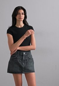 Camiseta negra ajustada combinada con una minifalda de mezclilla oscura de cintura alta que cuenta con un cierre de botones en la parte delantera y lazos para cinturón.