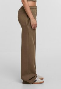 Khakifarbene Sweatpants mit lockerer Passform, elastischem Bund und seitlichen Taschen, aus einem glatten Baumwoll-Mischgewebe und mit geraden Beinen.
