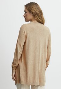 Lång, beige tröja i en mjuk, strukturerad stickning. Har en rund halsringning, neddragna axlar och sidoöppningar för ökad rörelsefrihet.
