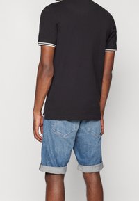 Černé polokošile s bílými pruhy na manžetách, doplněné světle modrými džínovými šortkami s ohrnutými lemy a zadními kapsami.