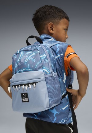 Sac à dos bleu à motif d'éclairs avec des accents gris, doté d'une poche zippée avant avec des graphismes de crocs, d'une poche latérale en mesh et de bretelles réglables.