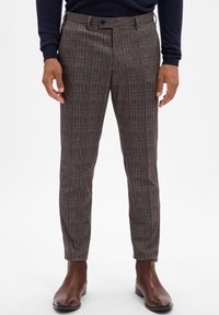 Checkered trousers in dark colors with a tailored fit, featuring subtle red and tan lines. Paired with brown leather boots.
