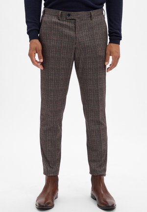 Pantaloni a scacchi in tonalità scure con una vestibilità su misura, caratterizzati da sottili linee rosse e beige. Abbinati a stivali in pelle marrone.