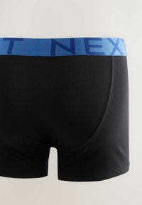 Fekete boxer nadrág kék elasztikus derékpánttal, amelyen a "NEXT" szó dús betűkkel szerepel; sima textúra és testhezálló fazon.