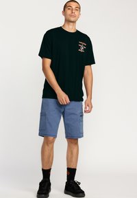 Sort bomulds t-shirt med grafisk tryk på forsiden, parret med lyseblå cargo shorts med dobbelte sidelommer. Sorte sneakers og ankelsokker fuldender looket.