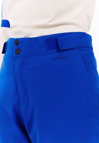 Blauwe skibroek met een gladde textuur, voorzien van twee zwarte knopen en een klittenbandstrip bij de taille. 'Protest' logo nabij de zak.