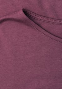 Gros plan d'une section pliée de tissu violet doux montrant une couture détaillée le long du bord.