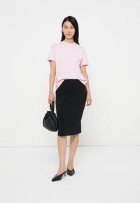 Ροζ κοντομάνικο μπλουζάκι συνδυασμένο με μια μαύρη εφαρμοστή μίνι φούστα. Το μοντέλο κρατά μια μαύρη πλισέ τσάντα και φορά μαύρες γόβες.