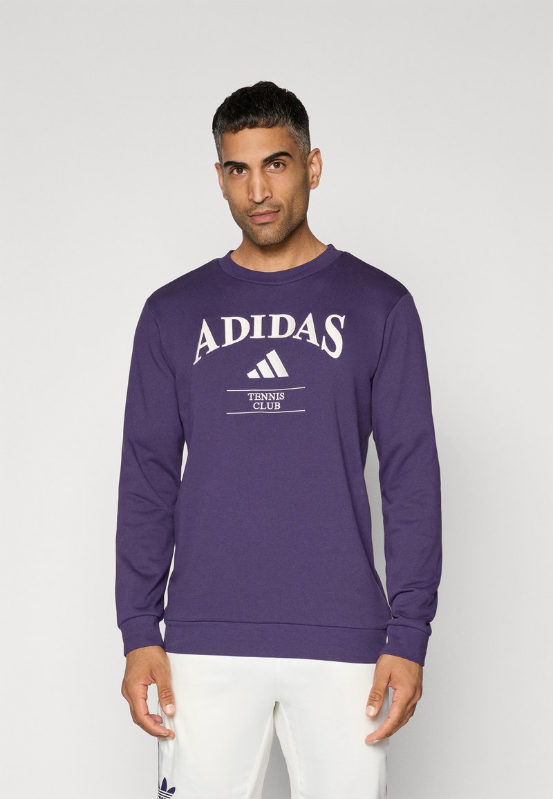 Lila, hosszú ujjú pulóver, fehér "ADIDAS TENNIS CLUB" logóval és három csíkkal a dizájnján, puha, texturált anyagból készült.