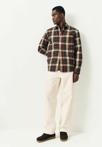 Kariertes Button-Down-Hemd in Rot, Grün und Creme, kombiniert mit cremefarbenen Hosen und schwarzen Schuhen. Das Hemd verfügt über zwei Brusttaschen und eine lockere Passform.