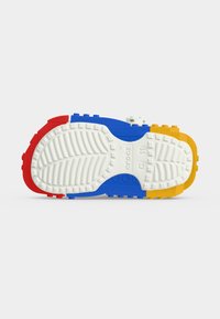 Σόλα πολύχρωμου παπουτσιού Crocs με κόκκινα, μπλε, κίτρινα τμήματα και λευκό πέλμα, δείχνοντας μέγεθος 9-10 και το ανάγλυφο όνομα της μάρκας.