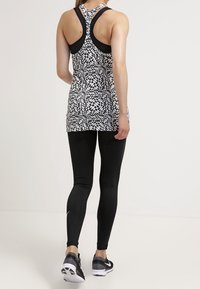 Dames zwart-wit geblokte sporttop met racerback ontwerp, gecombineerd met zwarte legging en sportschoenen met een gestructureerde zool.