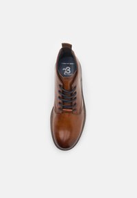 Botín de cuero marrón con un acabado suave, puntera redonda y cordones azul oscuro. Incluye un diseño de comodidad amplia para facilitar su uso.