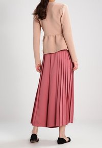 Dlouhá růžová plisovaná sukně spárovaná s texturovaným béžovým peplum topem; černé klopové baleríny dotvářejí celý outfit.