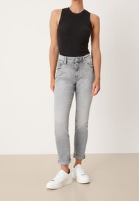 Top nero senza maniche, jeans a vita alta grigio chiaro e sneakers bianche. I jeans hanno una vestibilità standard con risvolti e tasche laterali.
