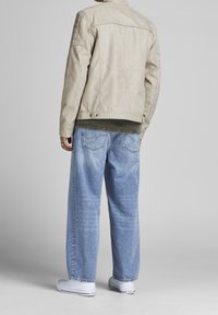 Beige faux kožená bunda s vysokým límcem, prošívanými detaily na ramenech, spárována s volnými světle modrými džíny a bílými teniskami.