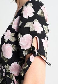 Schwarzes Kurzarmkleid mit pinkem Rosen- und grünem Blattmuster, das einen kleinen offenen Schlitz und ein gebundenes Stoffdetail am Ärmel aufweist.