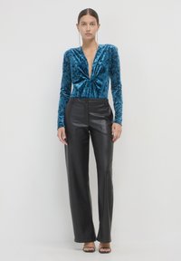 Body in velluto teal con scollatura a V profonda, maniche lunghe e texture liscia, abbinato a pantaloni in pelle neri a vita alta.