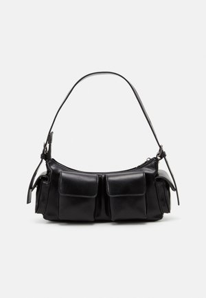 Zwarte leren handtas met een gebogen vorm, voorzien van twee steekzakken aan de voorkant en een smalle schouderriem. Gladde textuur en ritssluiting.