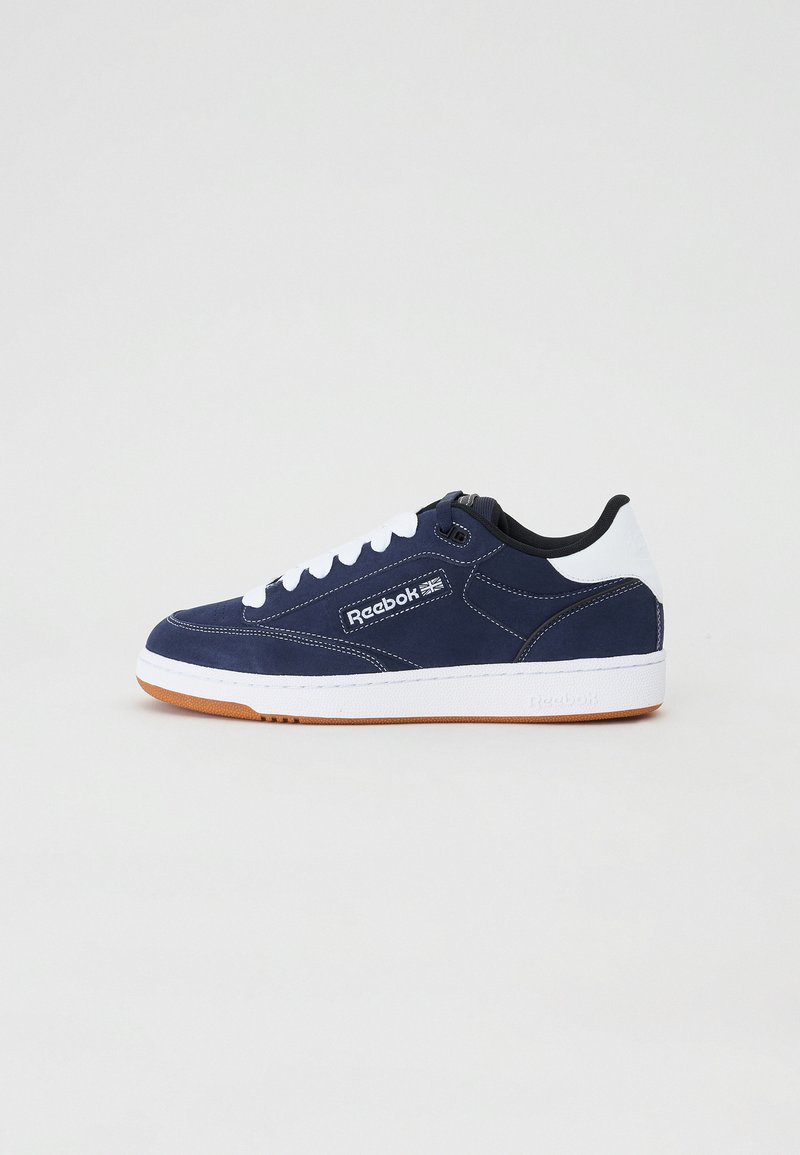 Navy blue sneaker with white accents, featuring a smooth suede upper, round toe, and rubber gum sole. Lace-up design with logo on side.