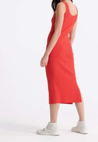 Neule, hihaton punainen midimekko, jossa on ribbikuviointi, tiukka siluetti ja sivuaukko, yhdistettynä valkoisiin korkean varren tennareihin.