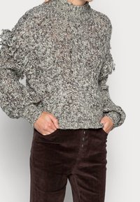 Chunky, gestructureerde gebreide trui in grijstinten met een hoge kraag en franjes op de mouwen, gecombineerd met bruine corduroy broek met knopen.