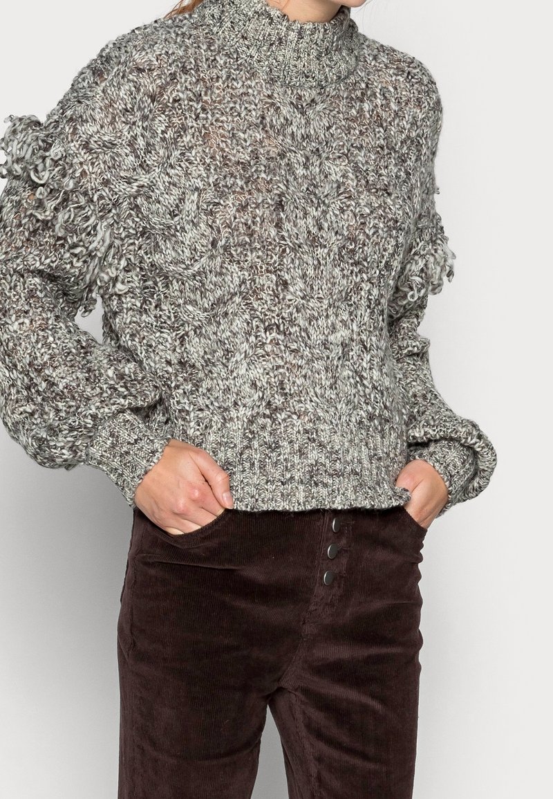 Chunky, gestructureerde gebreide trui in grijstinten met een hoge kraag en franjes op de mouwen, gecombineerd met bruine corduroy broek met knopen.