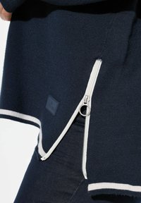 Dunkelblauer Pullover mit einem weißen Reißverschluss an der Seite, ausgestattet mit gerippten Saumakzenten und einem kleinen Markenschild auf der Vorderseite. Hergestellt aus weichem Material.