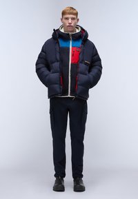 Puffer jacket with a navy exterior, red and blue accents on the inner lining, paired with dark pants and black boots. Textured, hooded design.