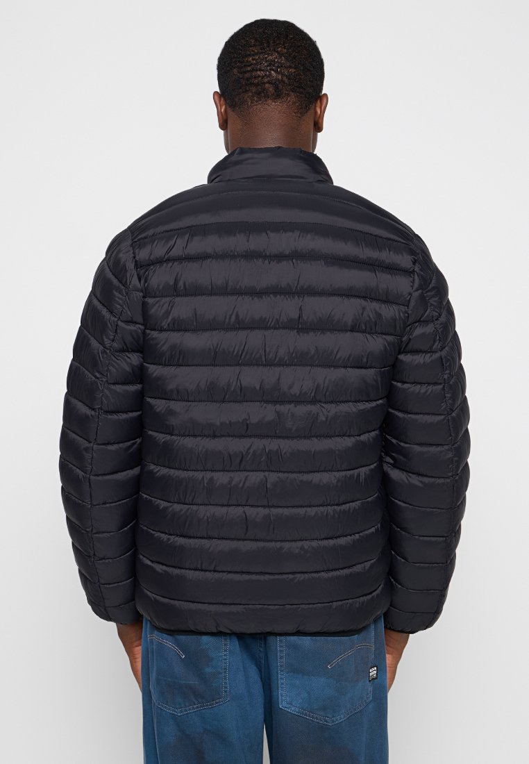 Veste noire rembourrée avec un design matelassé, col montant et poignets à côtes. Le matériau semble lisse et brillant avec des coutures horizontales.