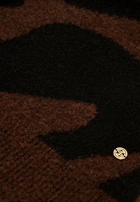 Tissu avec un motif brun et noir, d'une texture douce, comportant un petit accent de logo doré dans le coin.