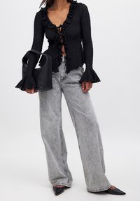 Sort struktureret cardigan med flæse-detaljer, åben front og lange ærmer. Sammenstylet med lysegrå bredbenede jeans og sorte spidse sko.