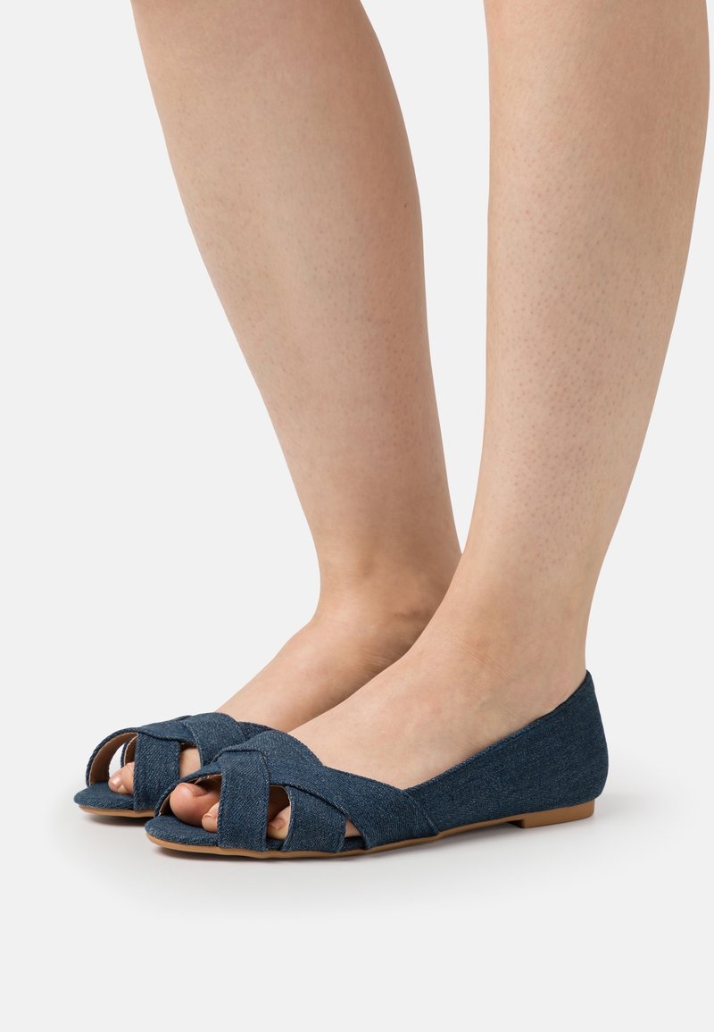 Ballerines en denim avec un design à bande croisée, bout ouvert, et semelle plate de couleur bleu foncé avec une finition en tissu texturé.