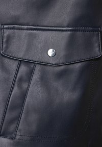 Marinblå läderficka med texturerad yta, som har en silvrig tryckknapp och distinkta sömmar längs kanterna för extra detalj.