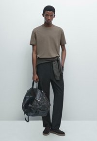 Hnědé bavlněné tričko spárované s volnými černými kalhotami, svetr uvázaný v pase a černá kožená sportovní taška.