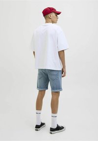 Hvid oversized t-shirt, lyseblå denim shorts med oprettede kanter, sorte sneakers og en rød kasket, set fra ryggen. Hvide sokker synlige.