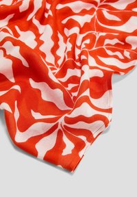 Rode en witte sjaal met een golvend, abstract patroon, gemaakt van zachte stof met een gladde textuur. In plooien gedrapeerd.