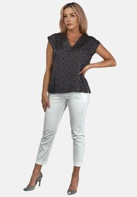 Czarna bluzka peplum w białe kropki z krótkimi rękawami, w połączeniu z białymi spodniami o dopasowanym kroju i srebrnymi szpilkami, charakteryzująca się gładką teksturą i nowoczesnym designem.