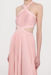 Robe plissée rose avec des bretelles croisées, des découpes à la taille et une jupe fluide. Texture lisse, tissu léger.