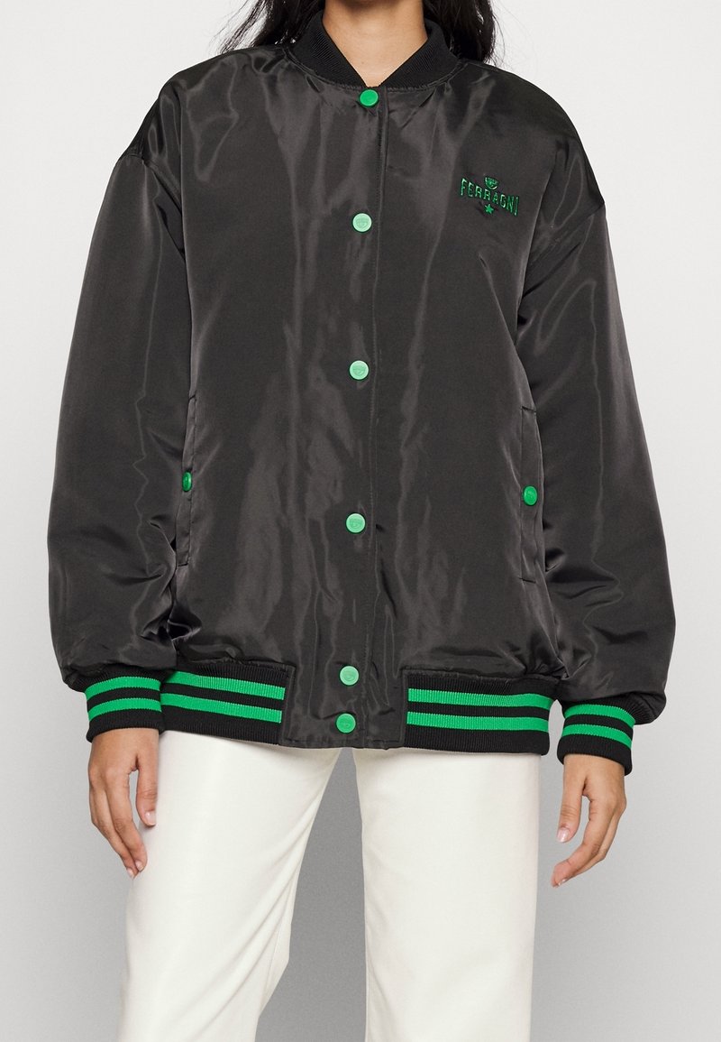 Svart satin bomberjacka med gröna tryckknappar och randiga ribbade ärmar och nederkant. Har broderad logotyp på bröstet.