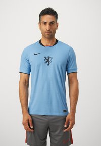 Maglia sportiva Nike di colore azzurro chiaro con un design texturizzato, logo di un leone nero e colletto e polsini delle maniche neri a contrasto.