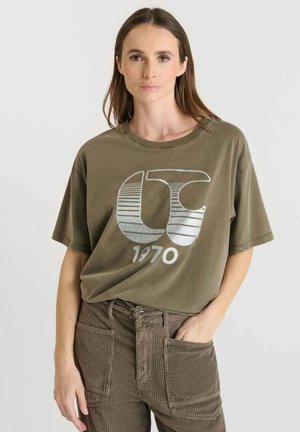 Olijfgroene katoenen t-shirt met een ronde hals, korte mouwen en een zilveren grafisch ontwerp met "CT 1970" op de voorkant.