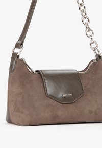 Brązowa torebka z zamszu i skóry o strukturalnym kształcie, z klapą, srebrnym okuciem i łańcuszkowym paskiem. Detal z zamkiem na górze.