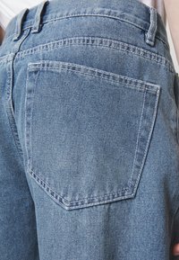 Jeans in denim azzurro chiaro con una grande tasca posteriore, Cuciture visibili e un design a vita alta. Il tessuto ha una texture morbida.